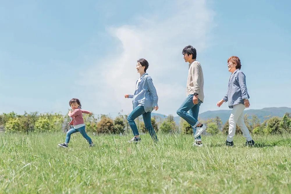 青空の下、草原で走る家族（健康で活動的な様子）