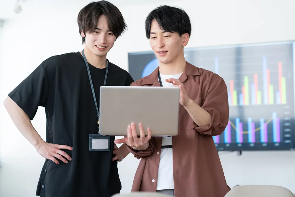 ノートパソコンを見ながら話す2人の若い男性