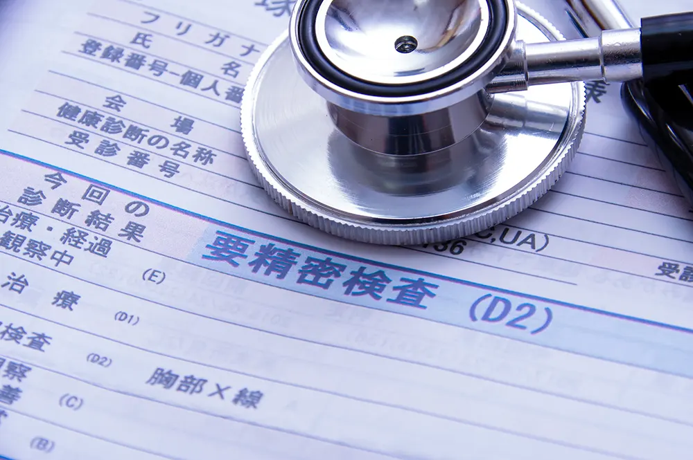 要精密検査と記された健康診断結果表の上に置かれた聴診器