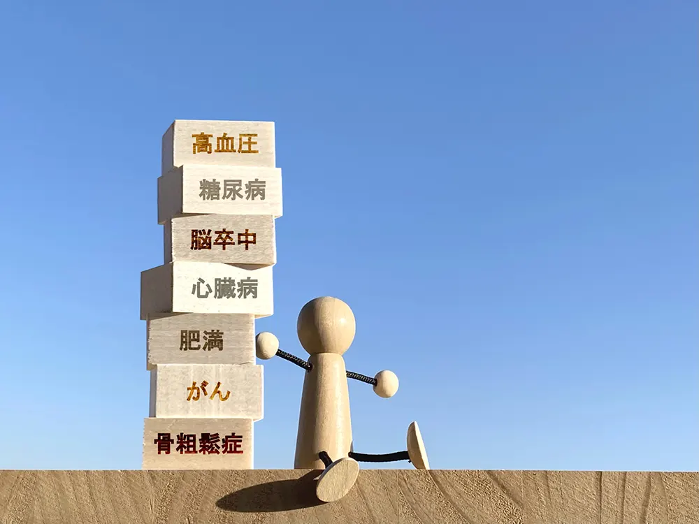 高血圧・糖尿病・脳卒中・心臓病・肥満・がん・骨粗鬆症と書かれた積み木を背負う人形(病気のリスク)