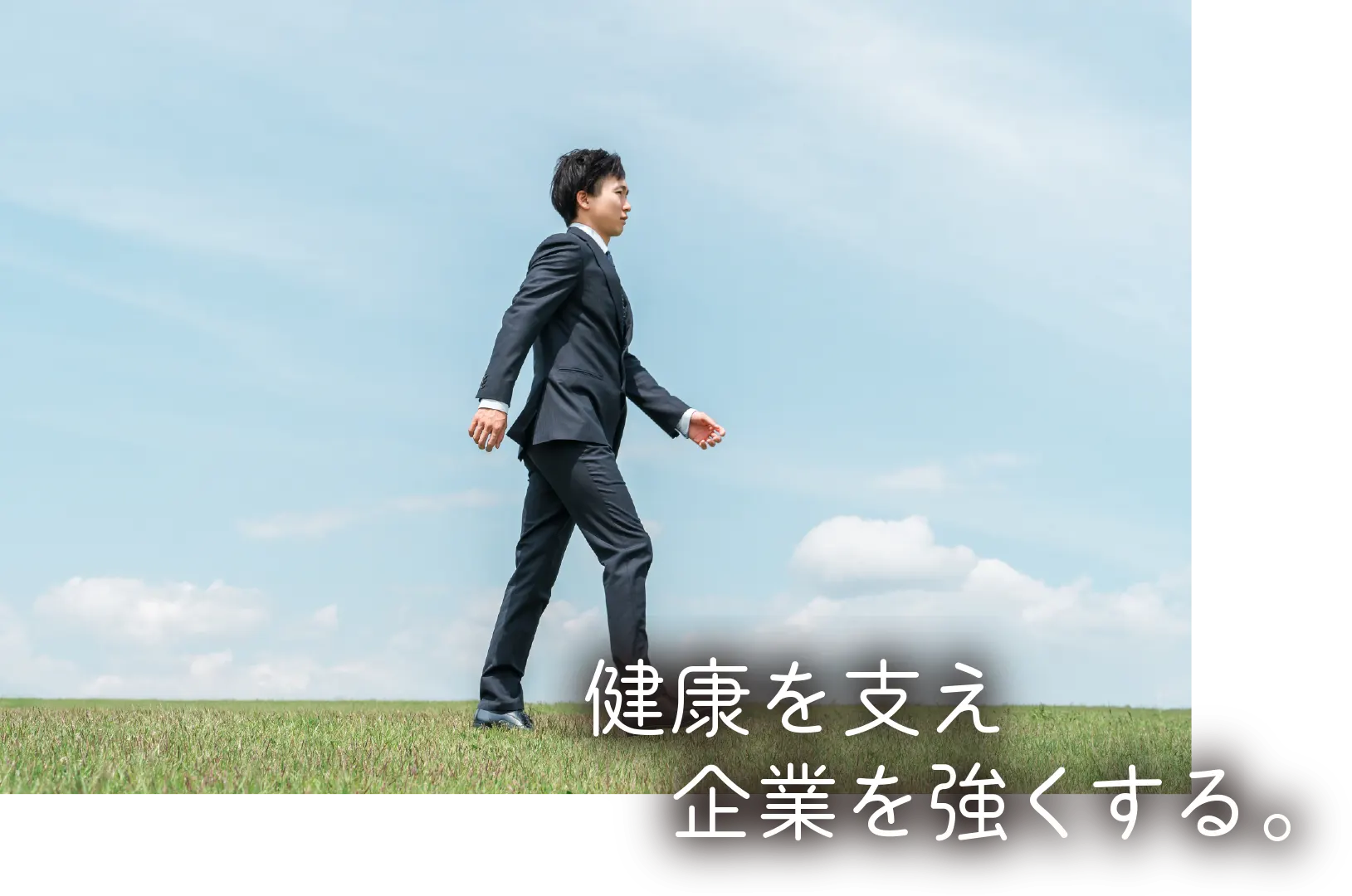 青空の下を歩くスーツ姿のビジネスマン（健康を支え、企業を強くする。）